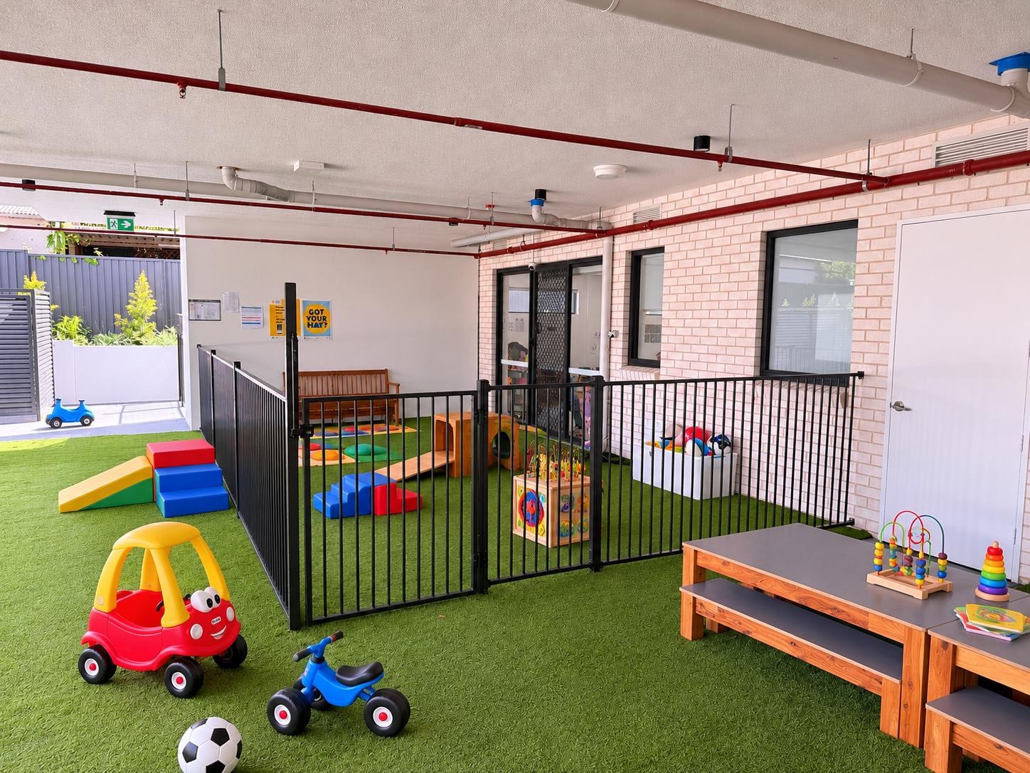 The covered baby play area at Campbelltown — soft turf, climbing blocks and toys inside a fully fenced enclosure
